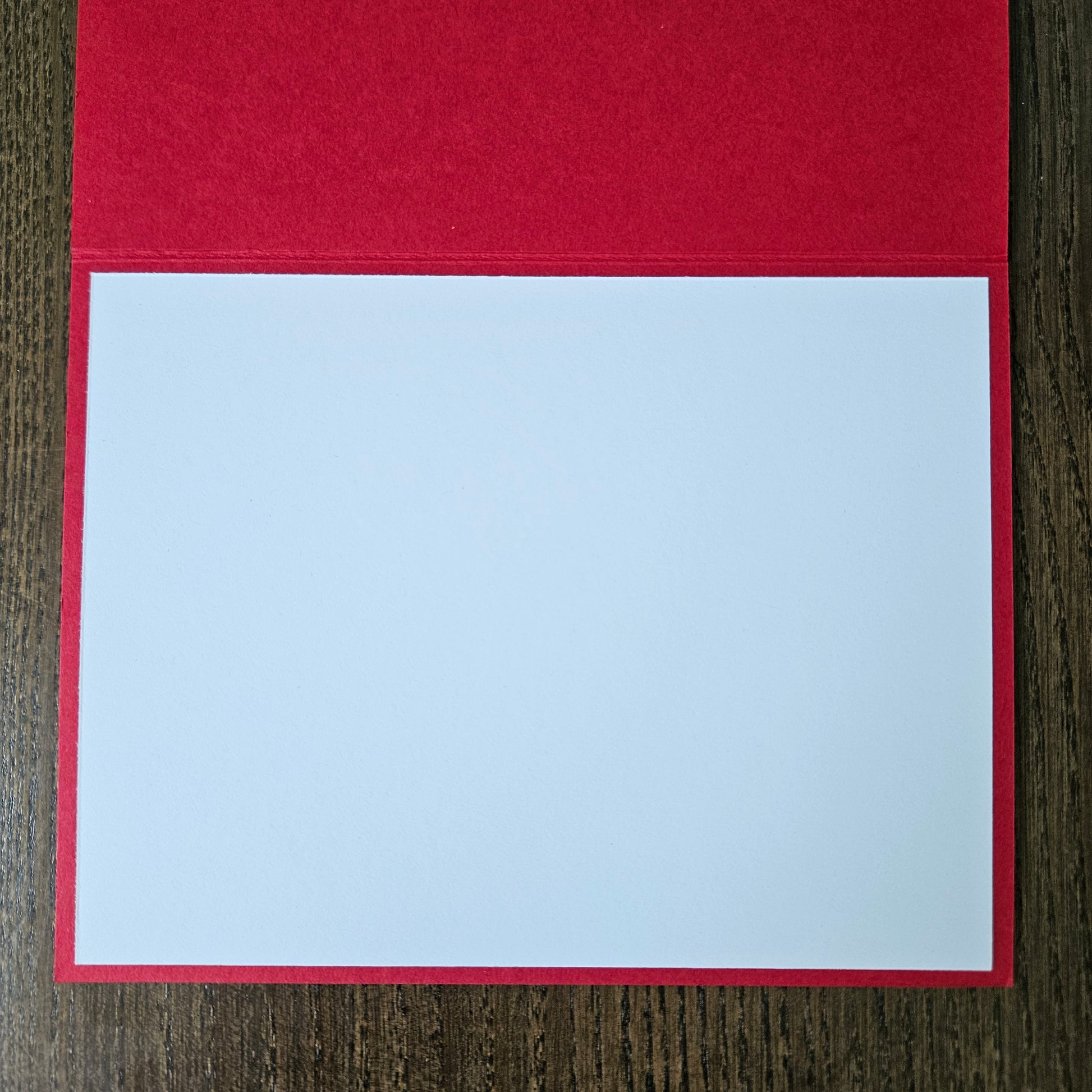 A blank white writing pad sheet with a red border, displayed open on a dark wood background.
