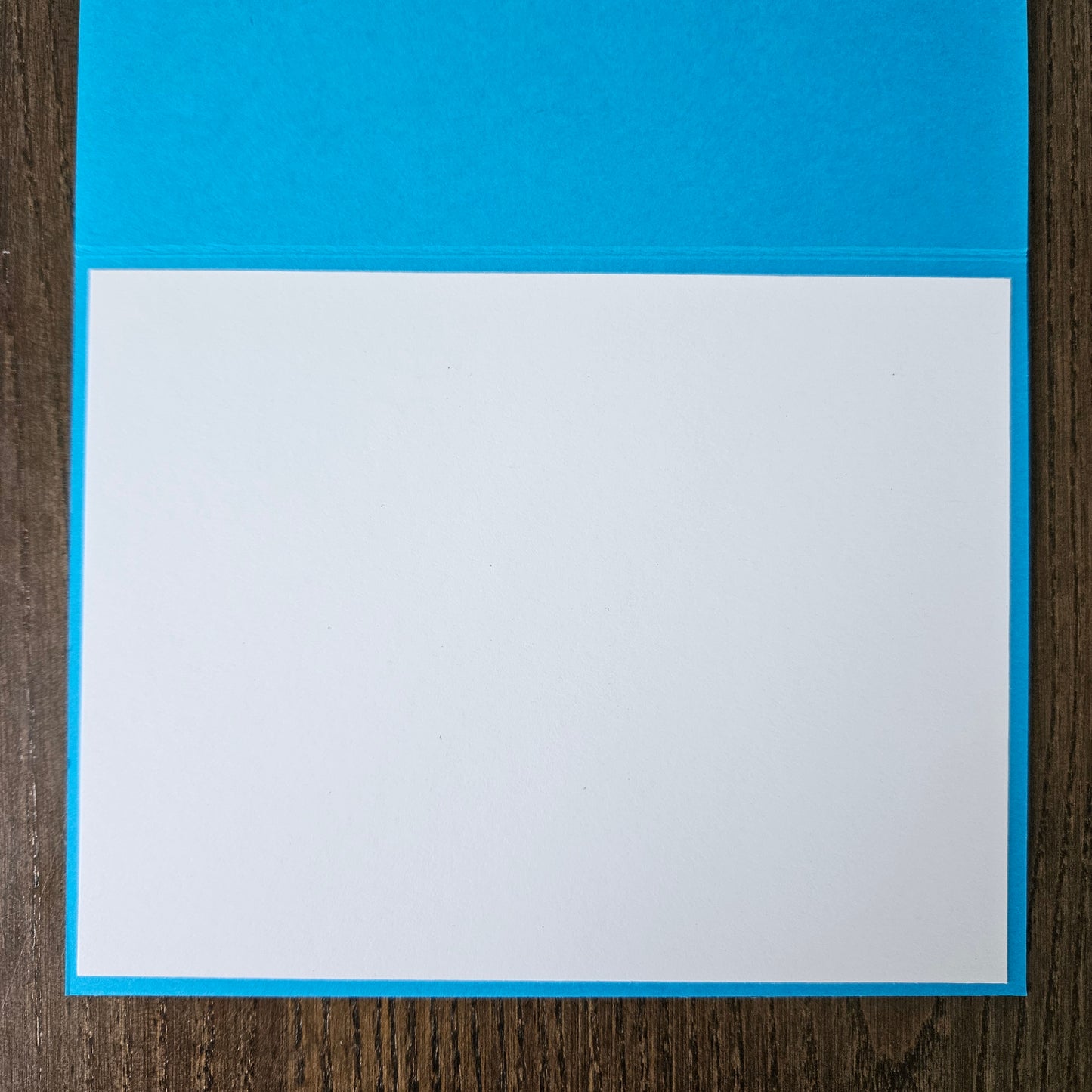 A square white card or paper sheet with a bright blue border, placed on a dark brown wood-grain surface.