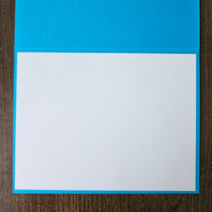 A square white card or paper sheet with a bright blue border, placed on a dark brown wood-grain surface.