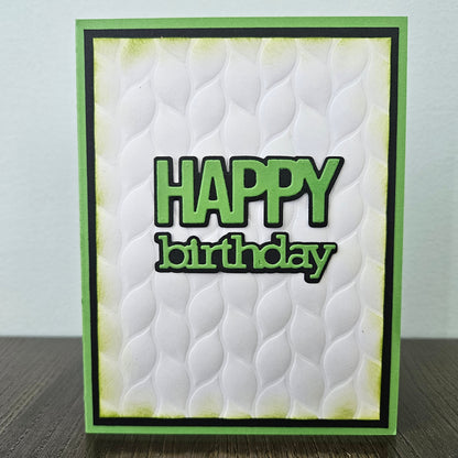 Front of the handmade 5x7 birthday card featuring an embossed white leaf-pattern background panel with hand-inked green edges, featuring bold die-cut text that reads HAPPY birthday in green with a crisp black outline, finished with a black inner mat and vibrant green cardstock