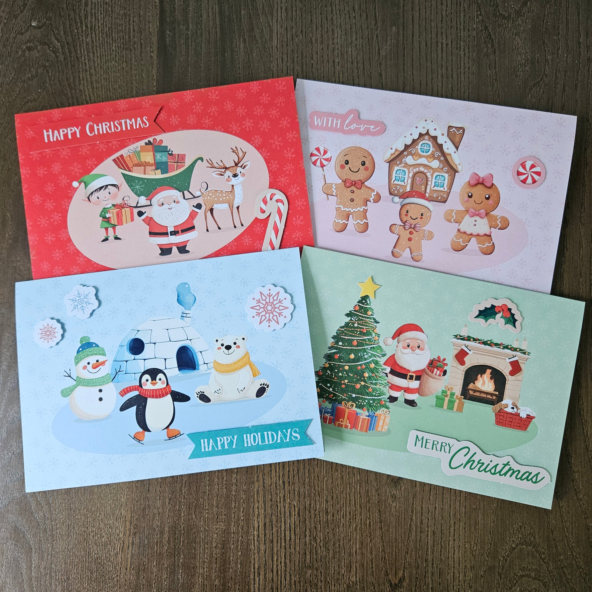 Four Christmas greeting cards arranged on a dark wood surface. The cards feature festive illustrations including Santa Claus, gingerbread people, a snowman, a polar bear, a Christmas tree, and holiday scenes, with text such as 'Happy Christmas,' 'With Love,' and 'Merry Christmas.