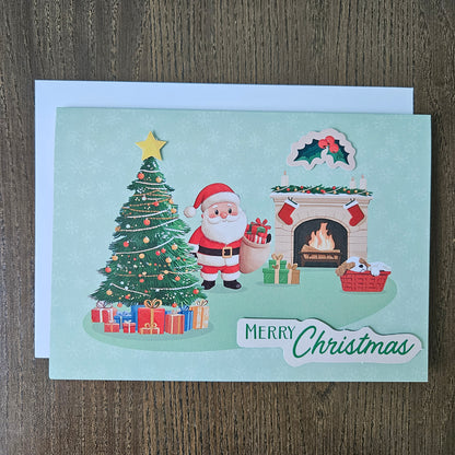 A Christmas greeting card featuring a festive illustration of Santa Claus by a decorated tree, gifts, a fireplace, and a 'Merry Christmas' banner, photographed on a wooden surface with a white envelope behind it.