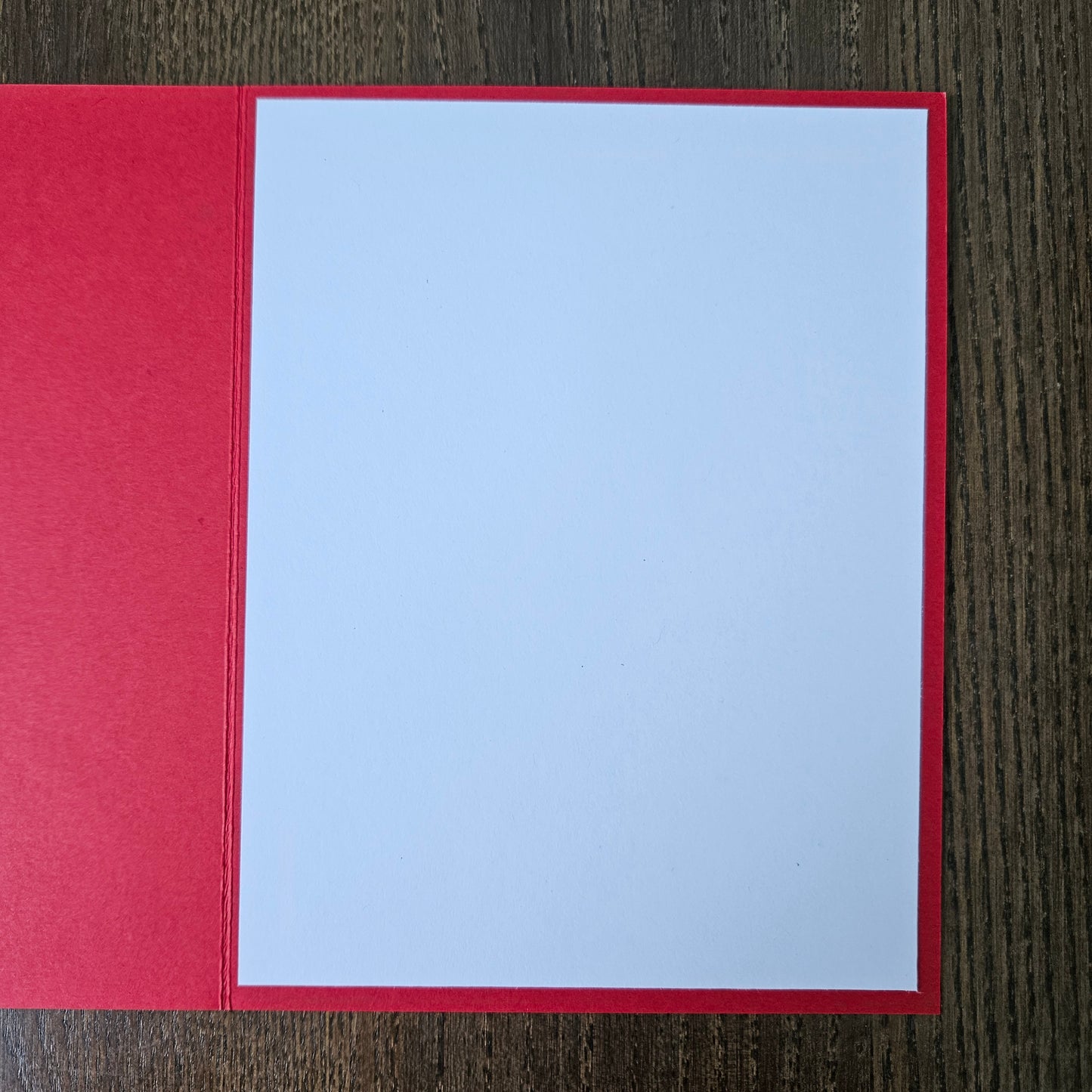 A blank white card centered on a red backing, photographed from above on a dark wood-grain surface.