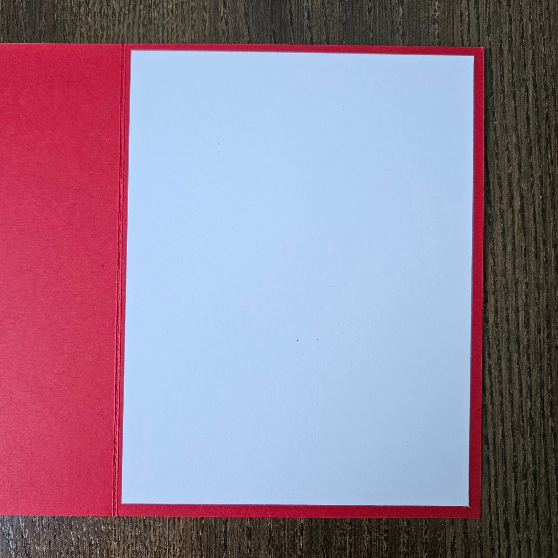 A blank white card centered on a red backing, photographed from above on a dark wood-grain surface.