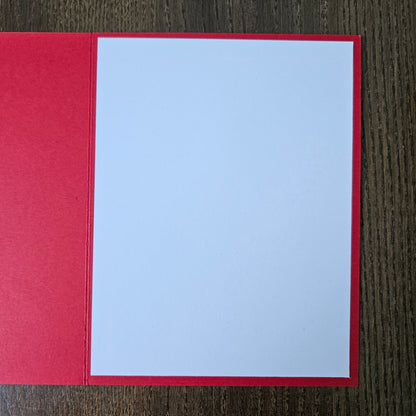 A blank white card centered on a red backing, photographed from above on a dark wood-grain surface.