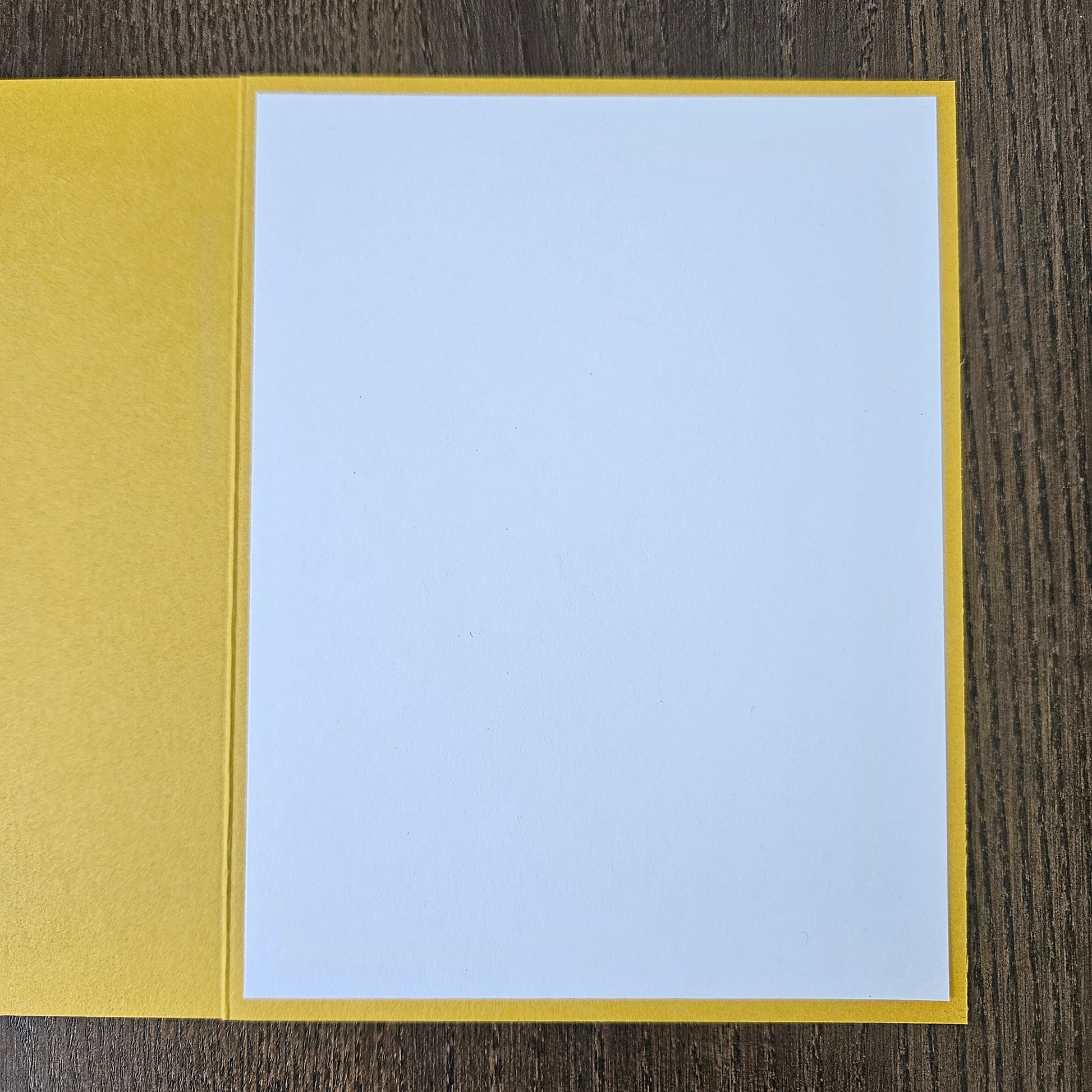 A blank white card or paper sheet with a yellow border, placed on a dark wood surface.