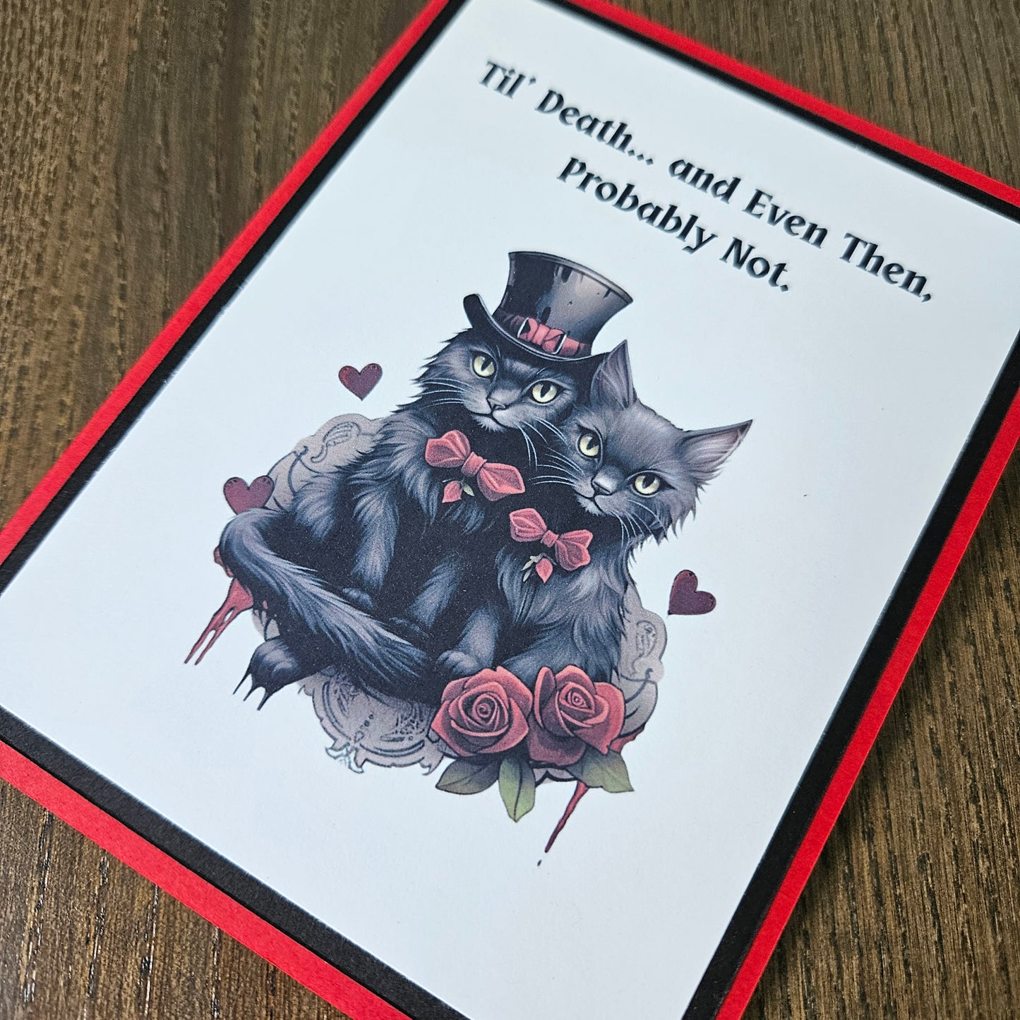 A square greeting card with a red border and black inner border, featuring an illustration of two black cats with pink bows and roses on a white background, with the text 'Till Death.