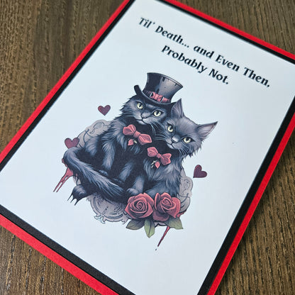 A square greeting card with a red border and black inner border, featuring an illustration of two black cats with pink bows and roses on a white background, with the text 'Till Death.