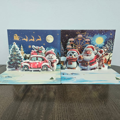 Two 3D pop-up Christmas greeting cards displayed side-by-side on a dark wooden table against a light gray wall. The left card features a snowy night scene with Santa Claus in a red car, a snowman, a Christmas tree, and sleighs.