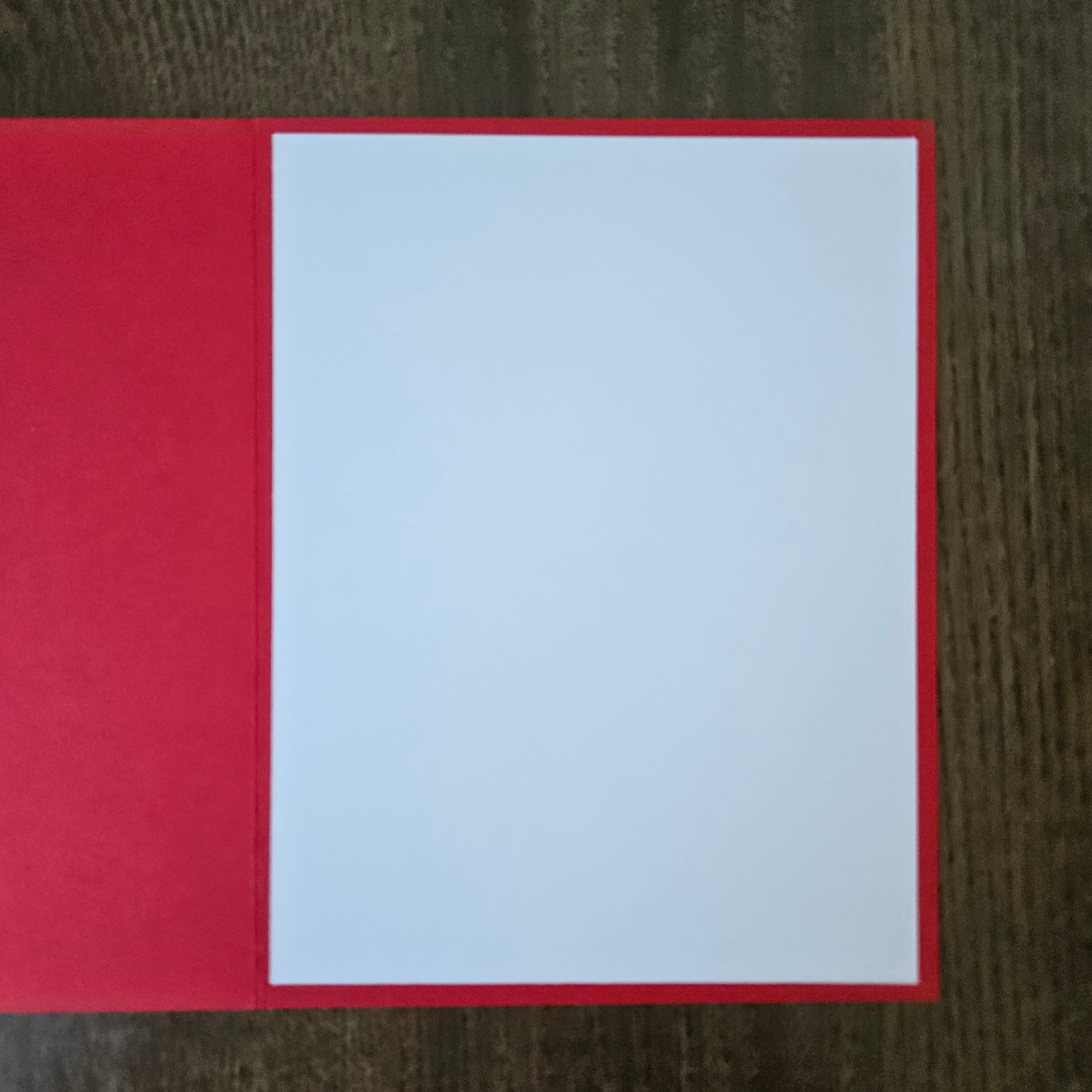 A red greeting card or paper folder with a blank white insert, photographed from above on a dark wood surface.