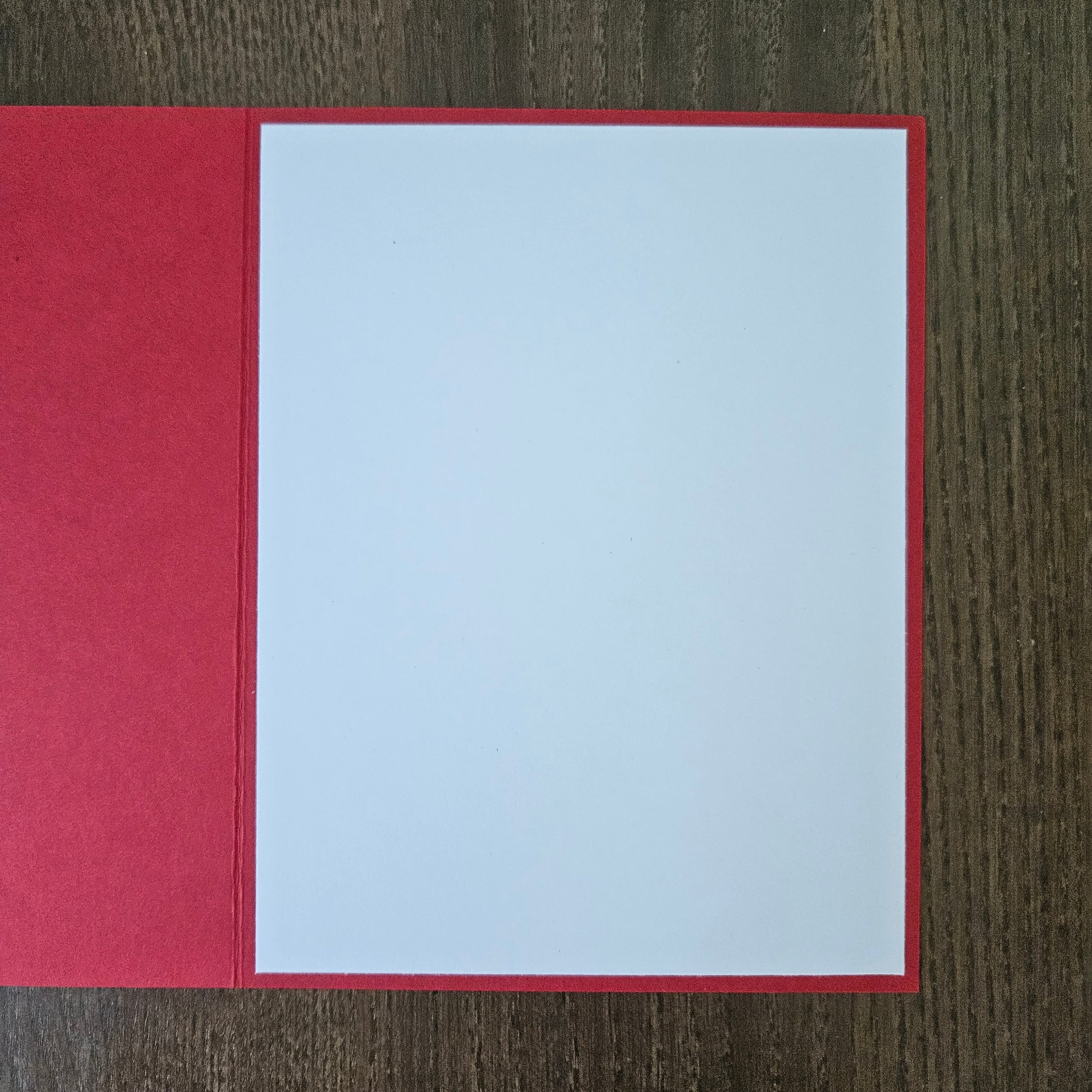 A red greeting card or envelope with a blank white insert, displayed flat on a dark wood background.