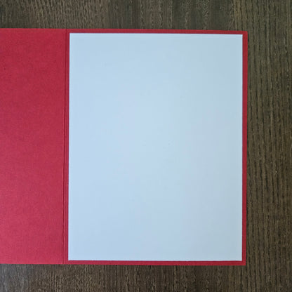 A red greeting card or envelope with a blank white insert, displayed flat on a dark wood background.