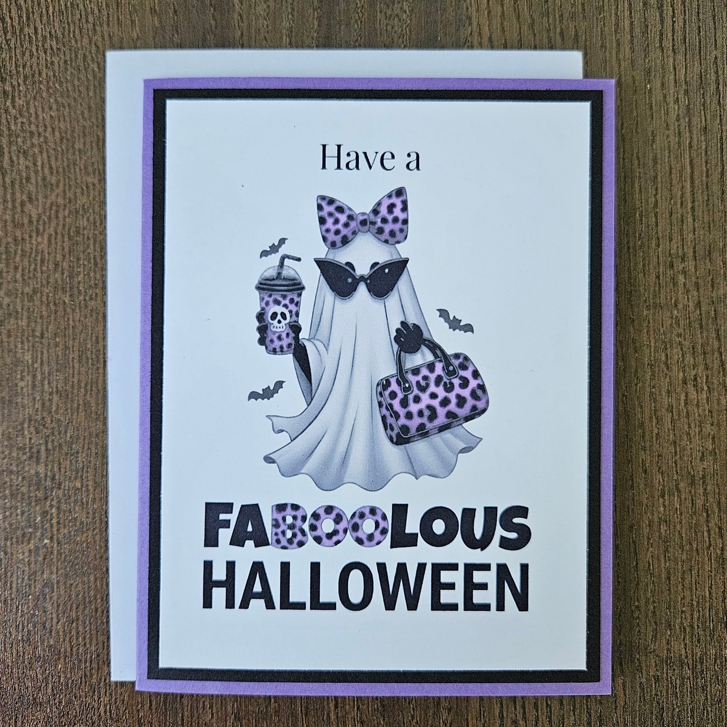 Front of a handmade A2 Halloween card featuring a layered purple and black border around a fashionable ghost wearing a purple leopard bow and sunglasses, holding an iced coffee and purse, with text reading Have a FABOOLOUS HALLOWEEN.