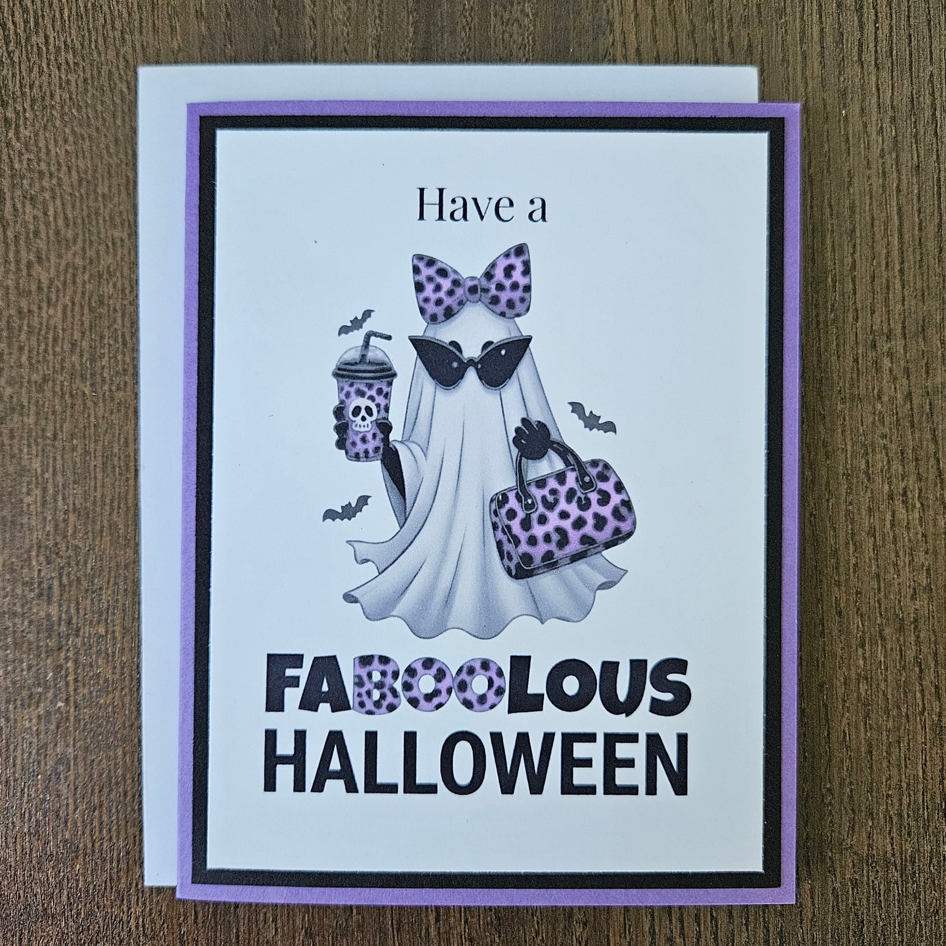 Front of a handmade A2 Halloween card featuring a layered purple and black border around a fashionable ghost wearing a purple leopard bow and sunglasses, holding an iced coffee and purse, with text reading Have a FABOOLOUS HALLOWEEN.