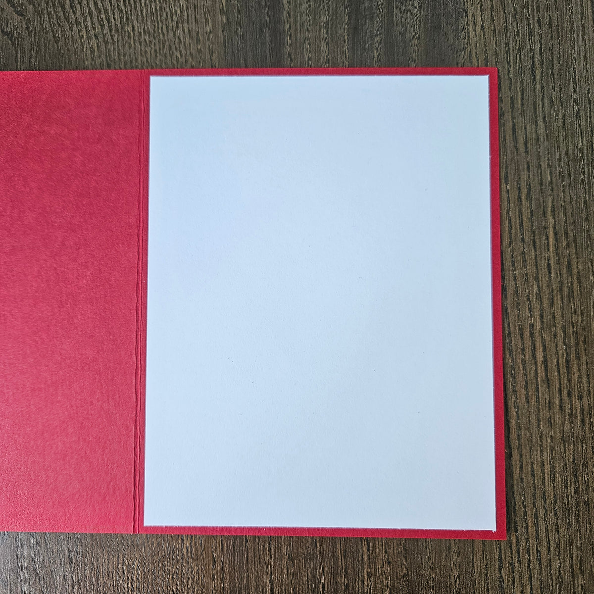 A red greeting card or envelope with a blank white insert, displayed flat on a dark wood-grain surface.