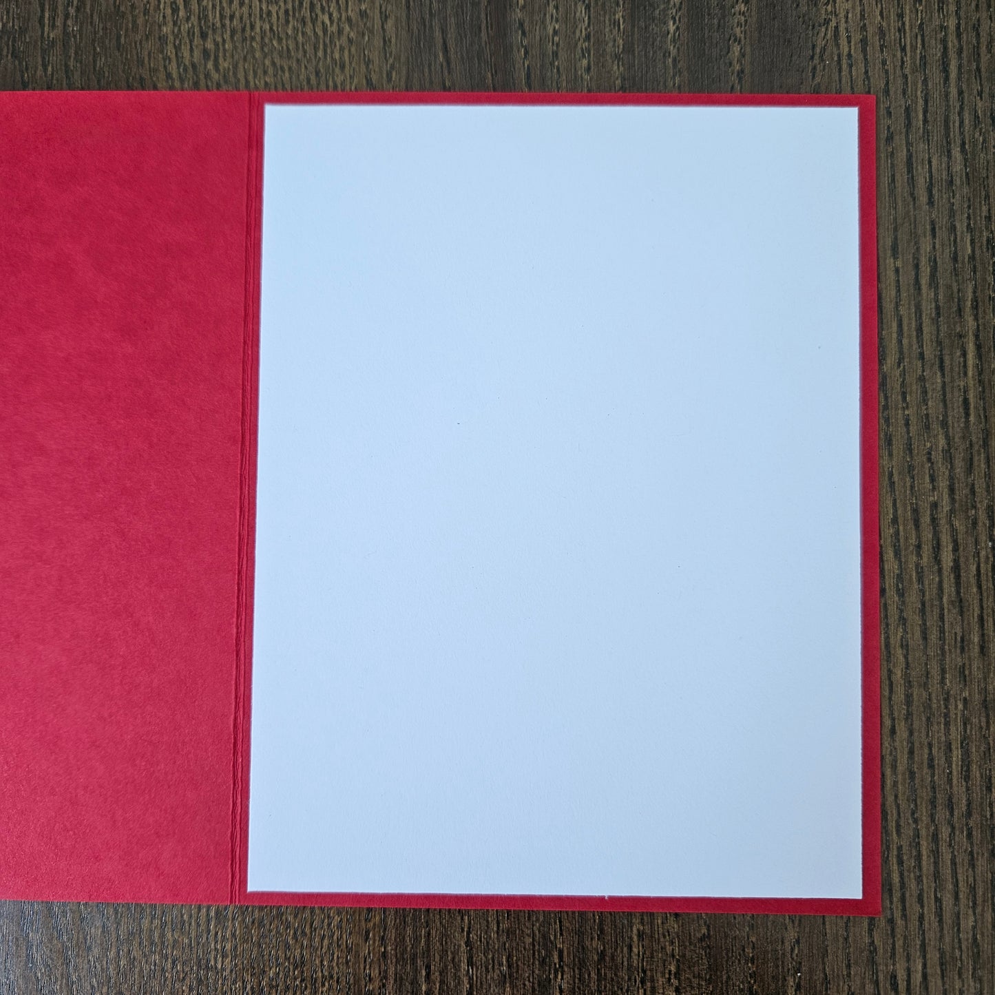 A red greeting card or envelope with a large blank white center panel, photographed flat on a dark wood surface.