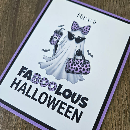 Front of a handmade A2 Halloween card featuring a layered purple and black border around a fashionable ghost wearing a purple leopard bow and sunglasses, holding an iced coffee and purse, with text reading Have a FABOOLOUS HALLOWEEN.