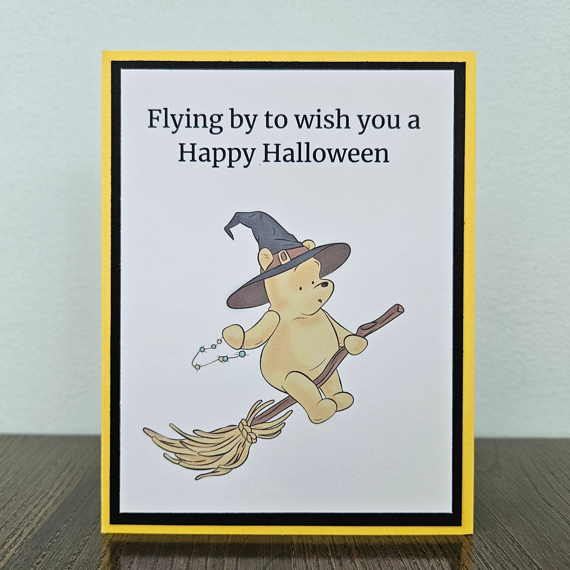 Front of a handmade A2 Winnie the Pooh Halloween card featuring Pooh Bear dressed as a witch flying on a broomstick with text reading Flying by to wish you a Happy Halloween.