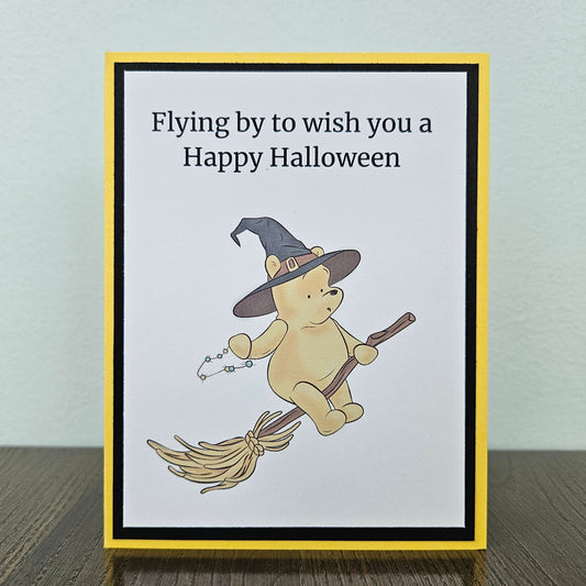 Front of a handmade A2 Winnie the Pooh Halloween card featuring Pooh Bear dressed as a witch flying on a broomstick with text reading Flying by to wish you a Happy Halloween.