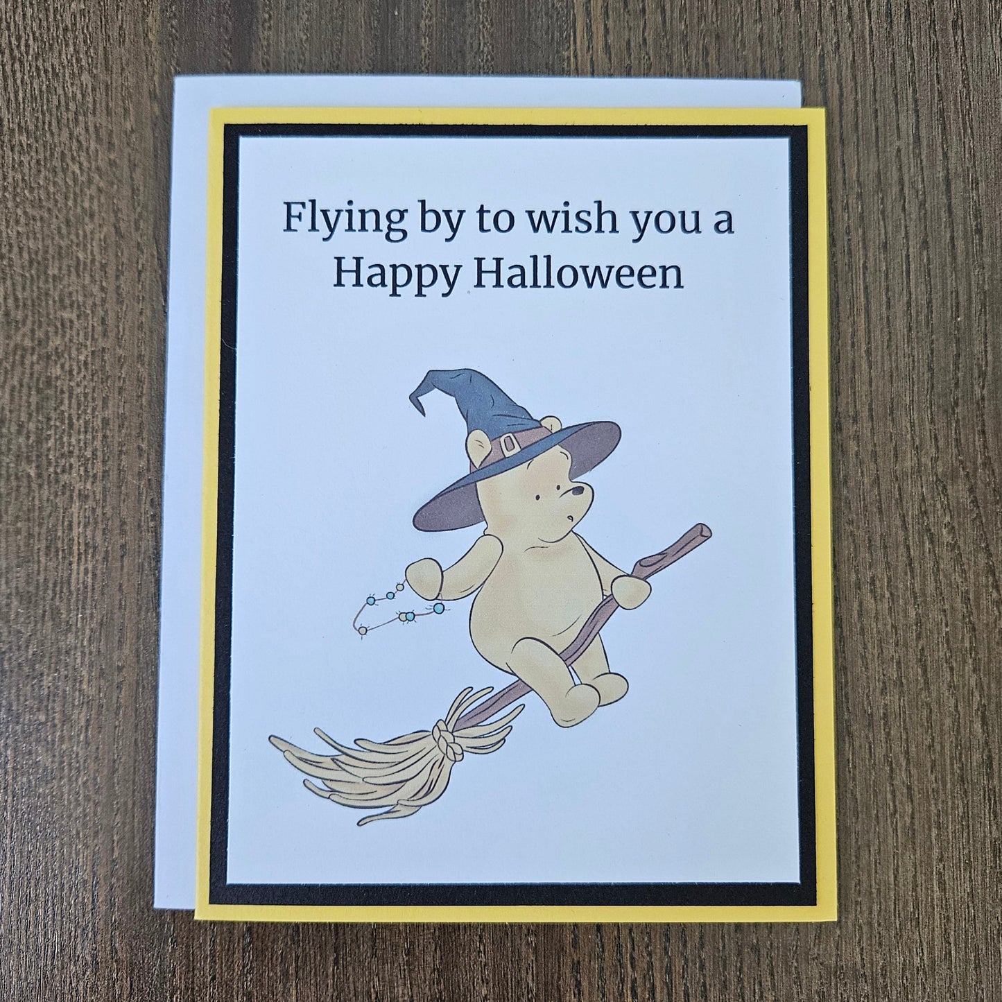 Front of a handmade A2 Winnie the Pooh Halloween card featuring Pooh Bear dressed as a witch flying on a broomstick with text reading Flying by to wish you a Happy Halloween.
