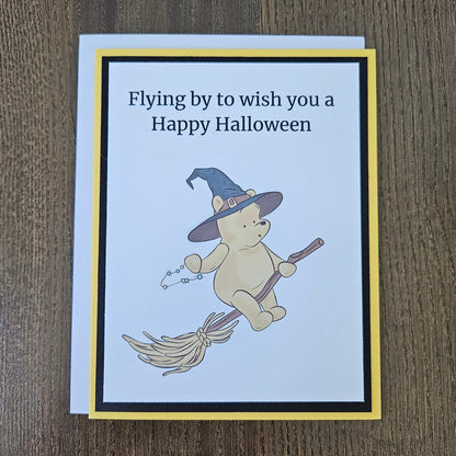 Front of a handmade A2 Winnie the Pooh Halloween card featuring Pooh Bear dressed as a witch flying on a broomstick with text reading Flying by to wish you a Happy Halloween.