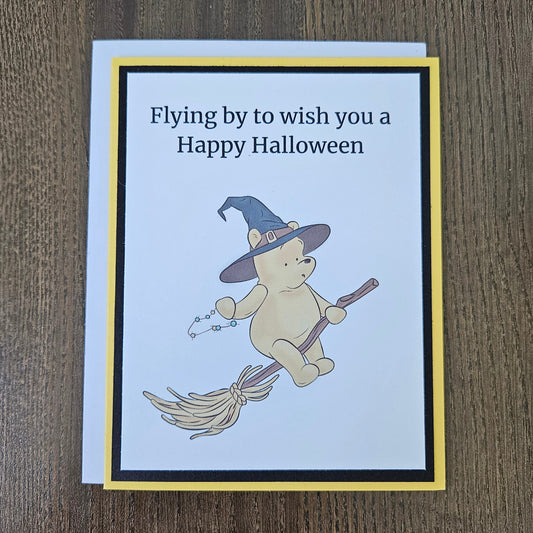Front of a handmade A2 Winnie the Pooh Halloween card featuring Pooh Bear dressed as a witch flying on a broomstick with text reading Flying by to wish you a Happy Halloween.