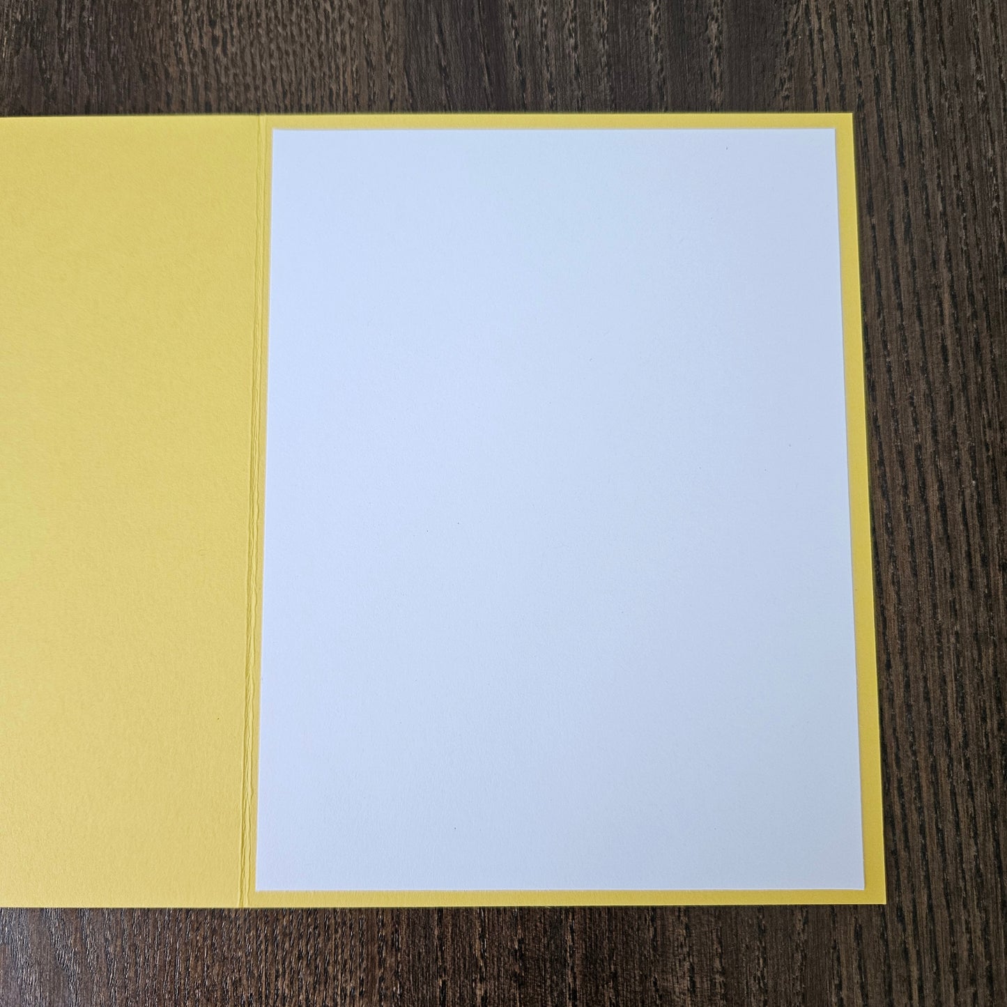 A blank white card centered on a yellow backing, laid flat on a dark wood-grained surface.