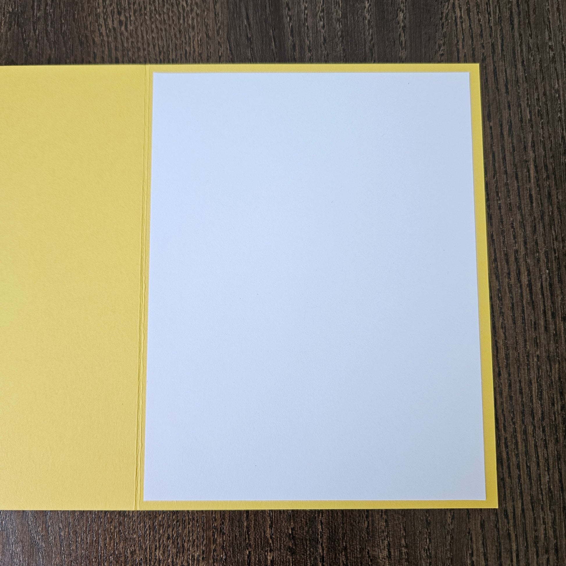 A blank white card centered on a yellow backing, laid flat on a dark wood-grained surface.