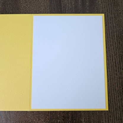 A blank white card centered on a yellow backing, laid flat on a dark wood-grained surface.