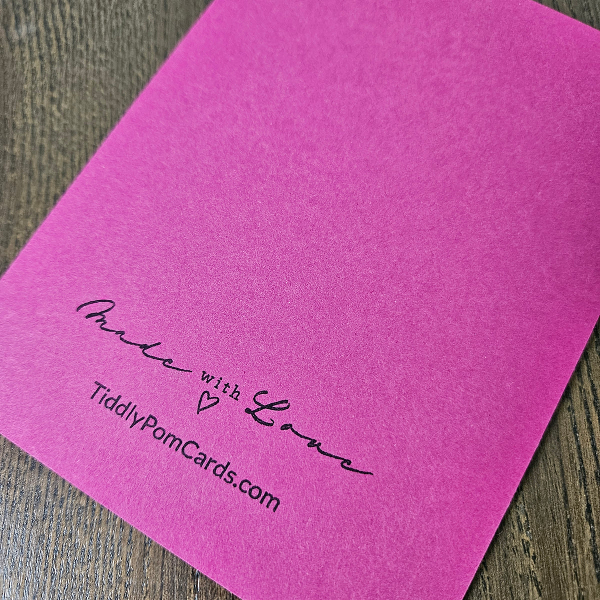 A square baby shower card with a floral design in pink, purple, and blue, featuring the text 'SOON, YOU WILL HOLD THE BABY GIRL WHO ALREADY HOLDS YOUR HEART.' on a wooden tabletop.
