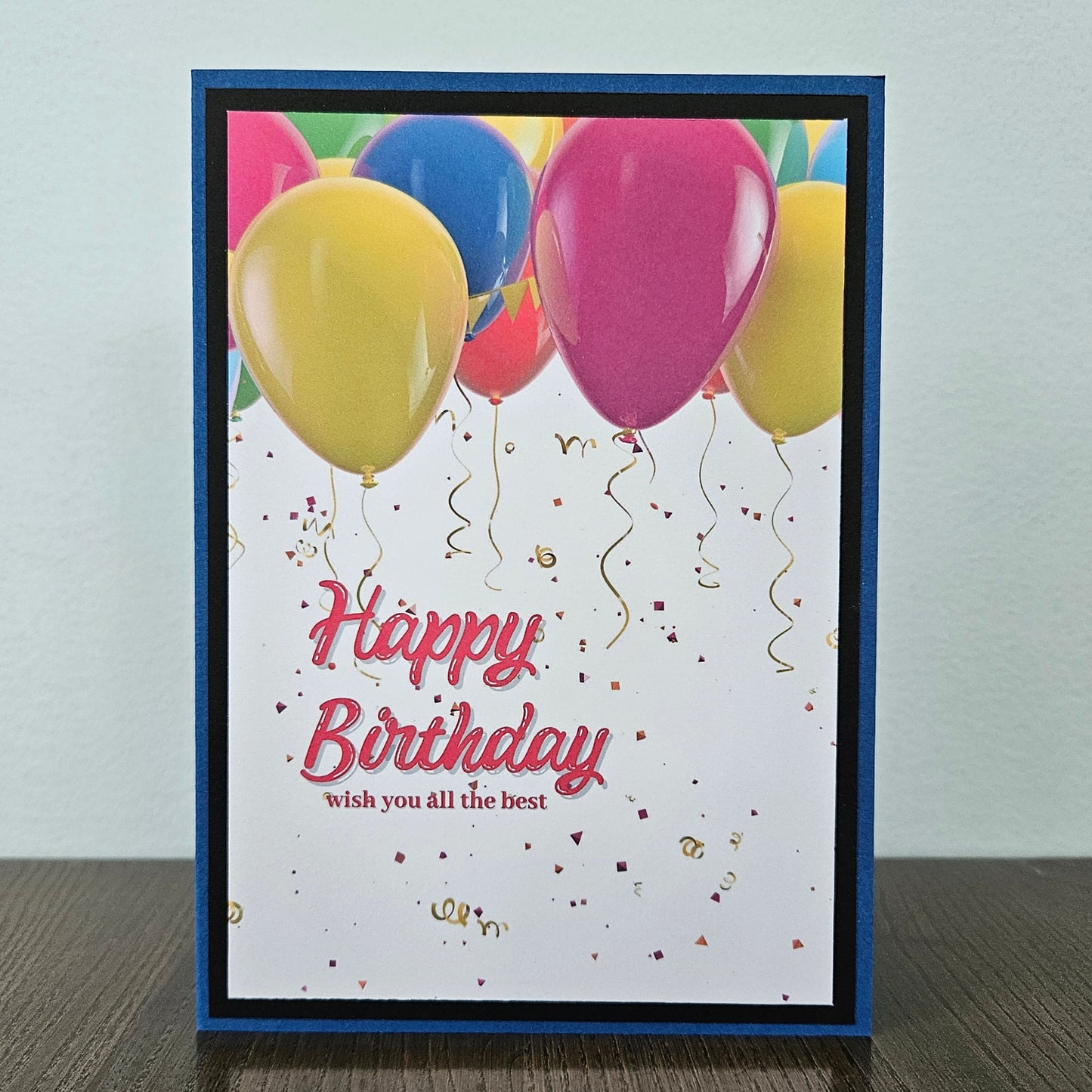 Front of a handmade A2 neutral birthday card featuring colorful balloons and gold confetti framed with layered borders and text reading Happy Birthday.