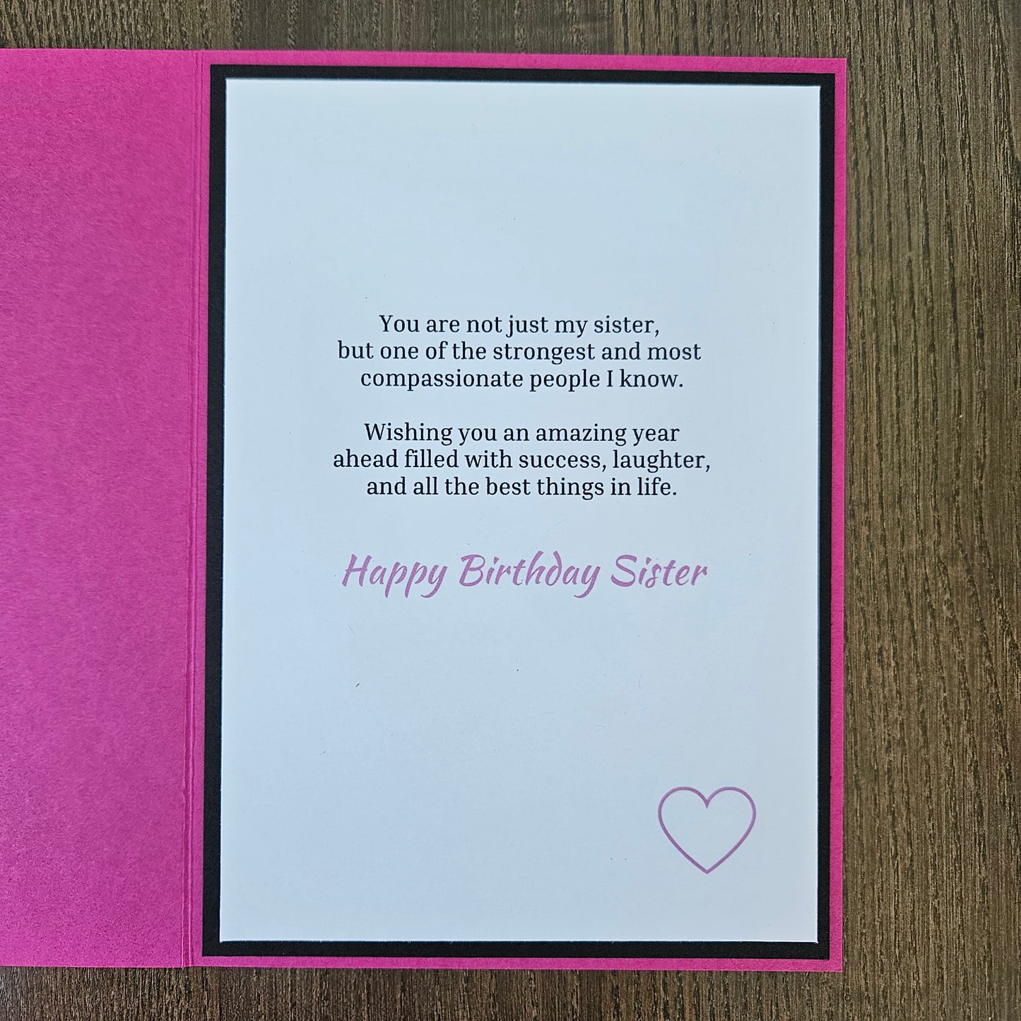A handmade birthday card for sister, featuring a bright pink textured cover and an open white card with black and pink text, placed on a brown wooden surface.