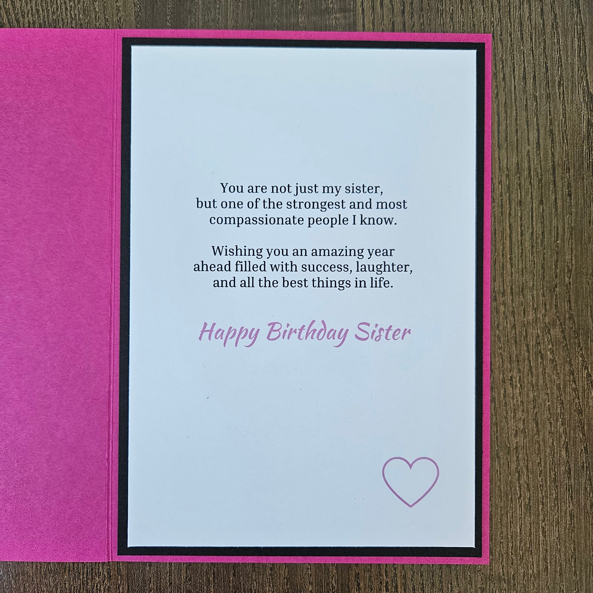 A handmade birthday card for sister, featuring a bright pink textured cover and an open white card with black and pink text, placed on a brown wooden surface.