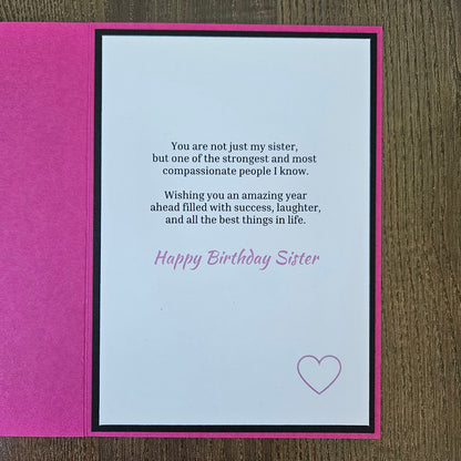 A handmade birthday card for sister, featuring a bright pink textured cover and an open white card with black and pink text, placed on a brown wooden surface.