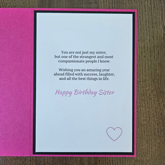 A handmade birthday card for sister, featuring a bright pink textured cover and an open white card with black and pink text, placed on a brown wooden surface.