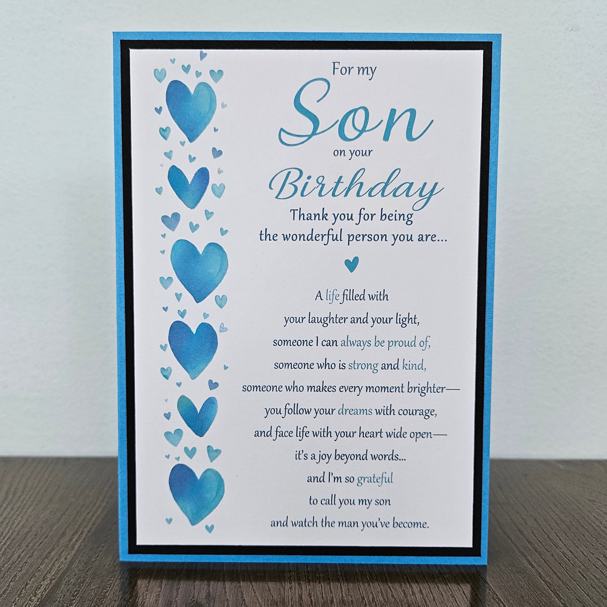 Front of a handmade 5x7 birthday card for son featuring a vertical row of watercolor blue hearts framed in black and blue with a detailed birthday poem.