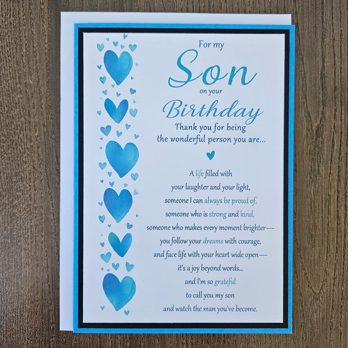 Front of a handmade 5x7 birthday card for son featuring a vertical row of watercolor blue hearts framed in black and blue with a detailed birthday poem.