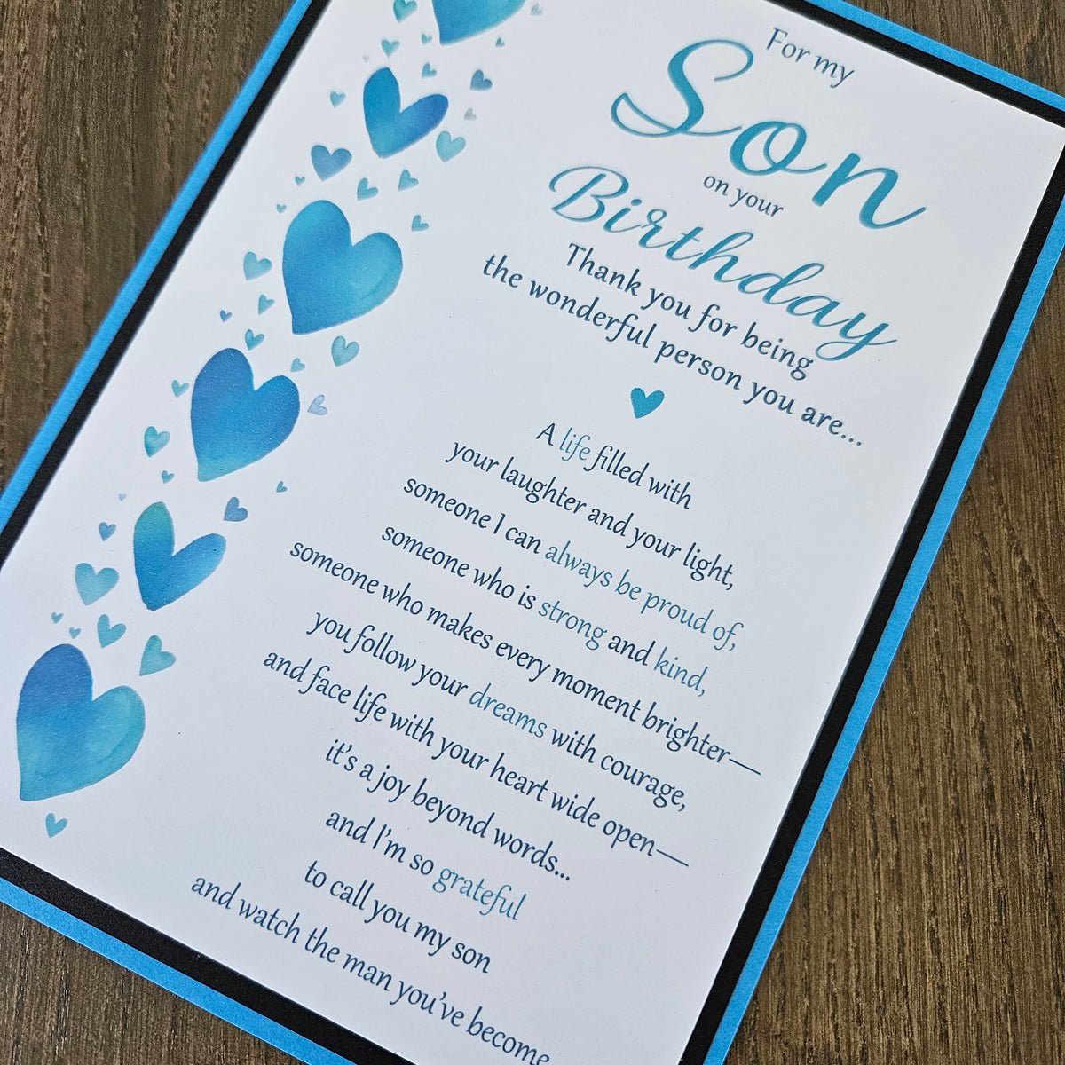 Front of a handmade 5x7 birthday card for son featuring a vertical row of watercolor blue hearts framed in black and blue with a detailed birthday poem.