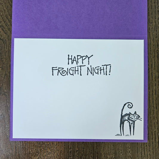 A square greeting card with a purple envelope, featuring the text 'HAPPY FROIGHT NIGHT!' in a hand-drawn black font and a small black cat illustration in the bottom right corner, displayed on a wooden surface.
