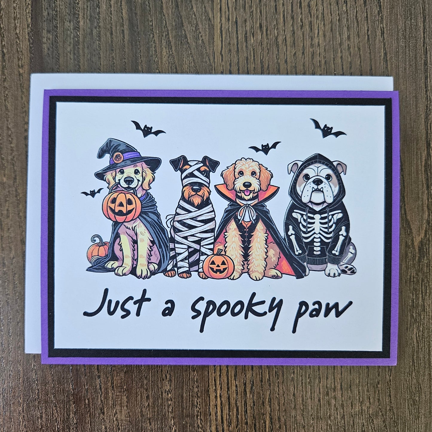 Front of a handmade A2 Halloween card featuring four dogs in Halloween costumes framed with black and purple borders with text reading Just a spooky paw.
