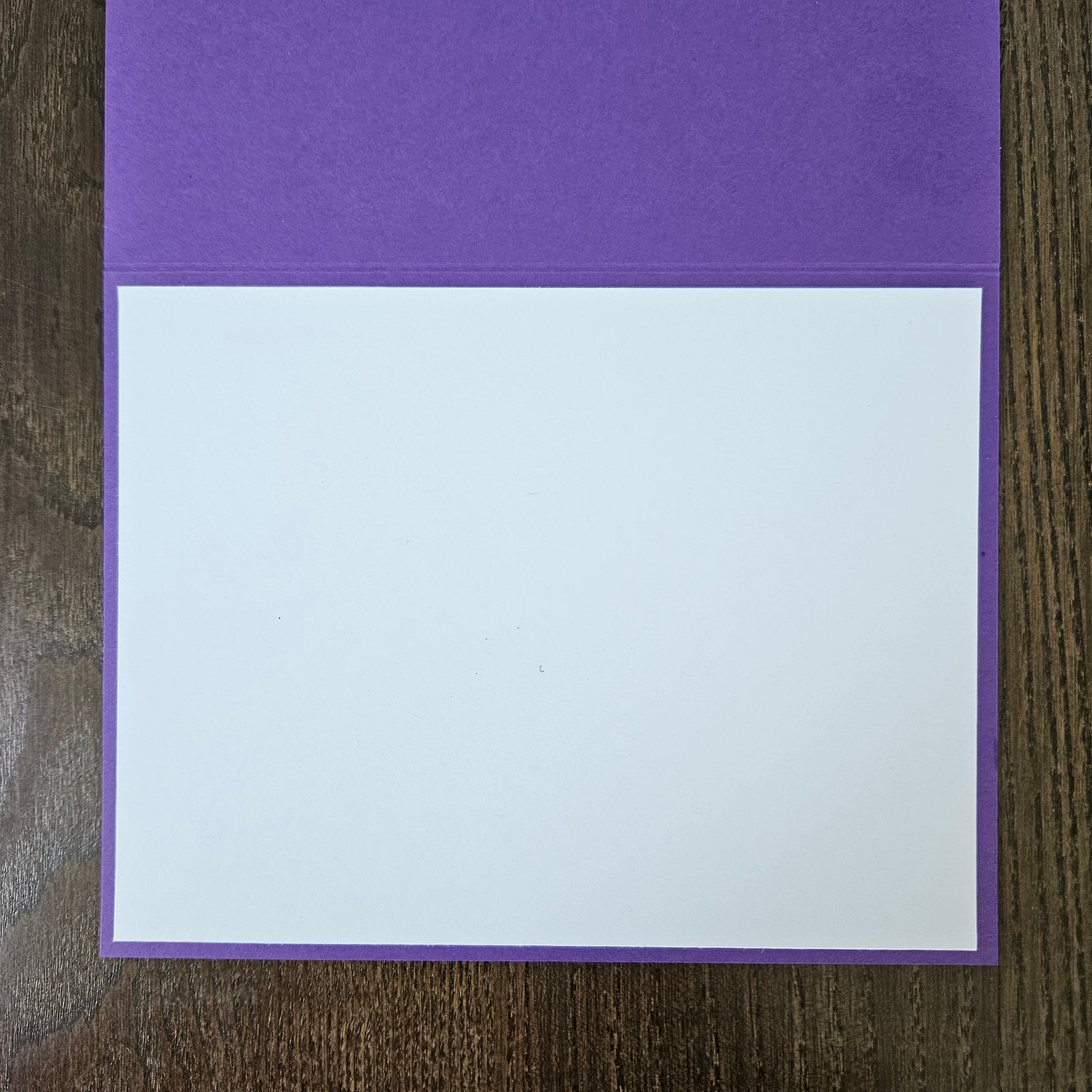 A purple card envelope or pocket folder with a blank white insert card, displayed flat on a dark wood background.