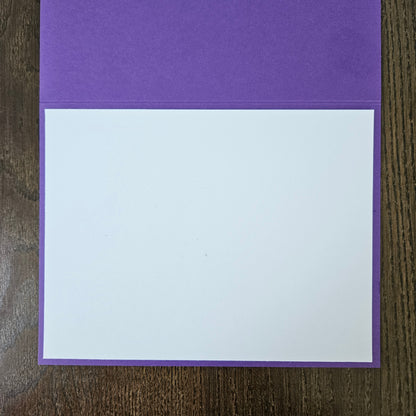 A purple card envelope or pocket folder with a blank white insert card, displayed flat on a dark wood background.
