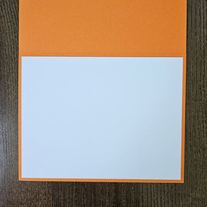 An orange folder or notebook cover with a large white page insert, photographed from above on a dark wood surface.