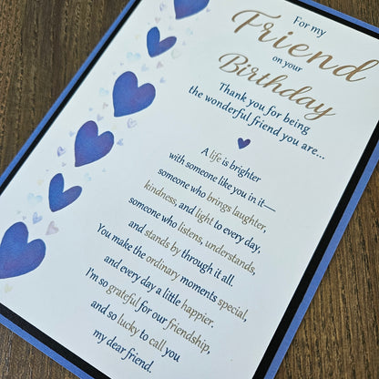A square printed card with a blue border and a poem for a friend's birthday, decorated with blue heart illustrations, shown on a wooden surface.