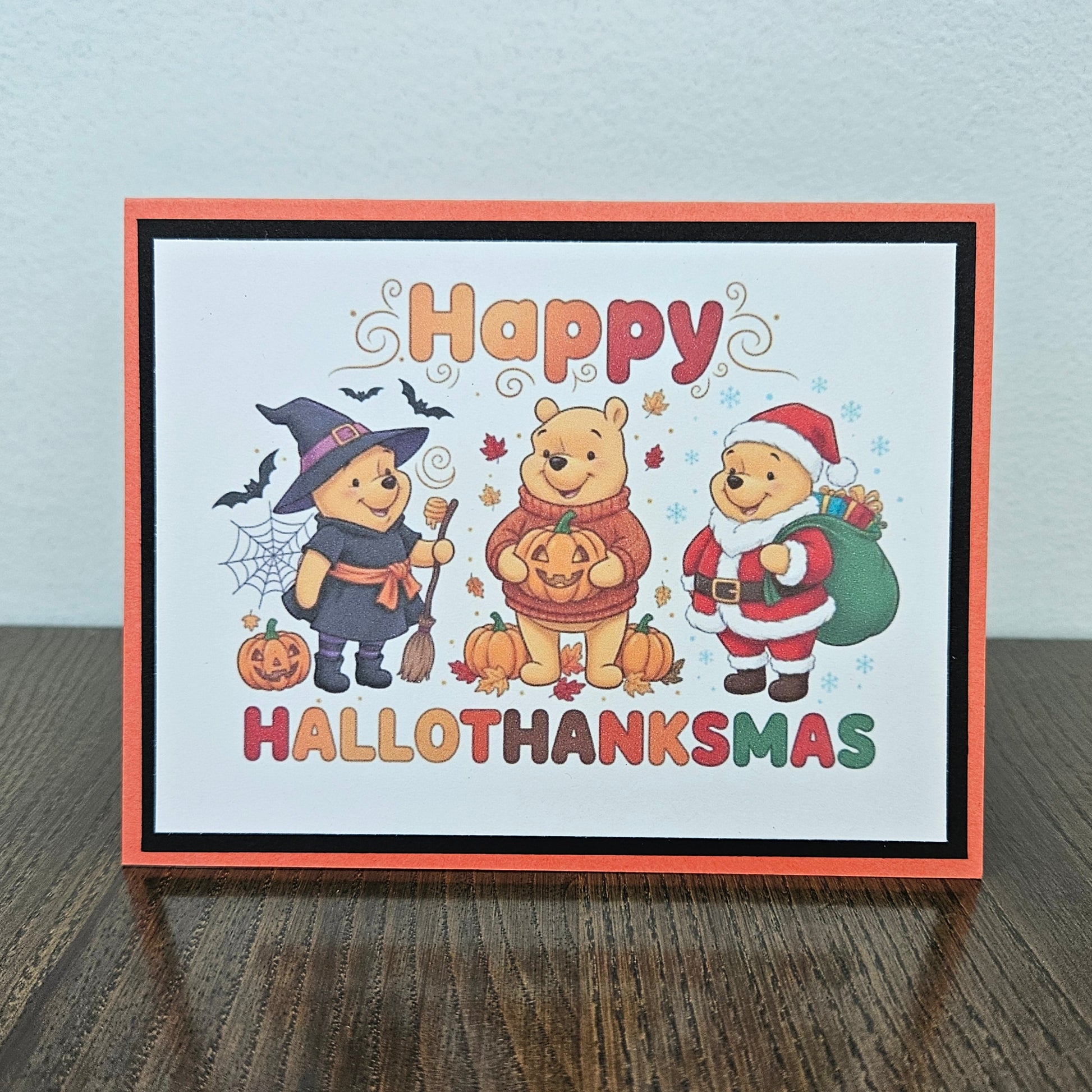 A greeting card with a Halloween and Thanksgiving holiday design, featuring Winnie the Pooh characters in costume, placed on a dark wooden surface against a light gray wall.