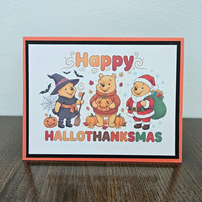 A greeting card with a Halloween and Thanksgiving holiday design, featuring Winnie the Pooh characters in costume, placed on a dark wooden surface against a light gray wall.