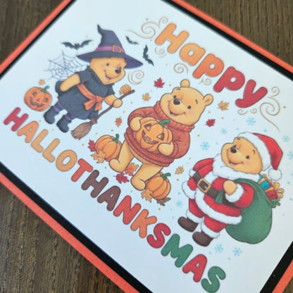 A square printed card featuring Winnie the Pooh characters in Halloween Thanksgiving outfits, with the text 'Happy HALLOTHANKSMAS' on a white background with an orange border, photographed on a wooden surface.