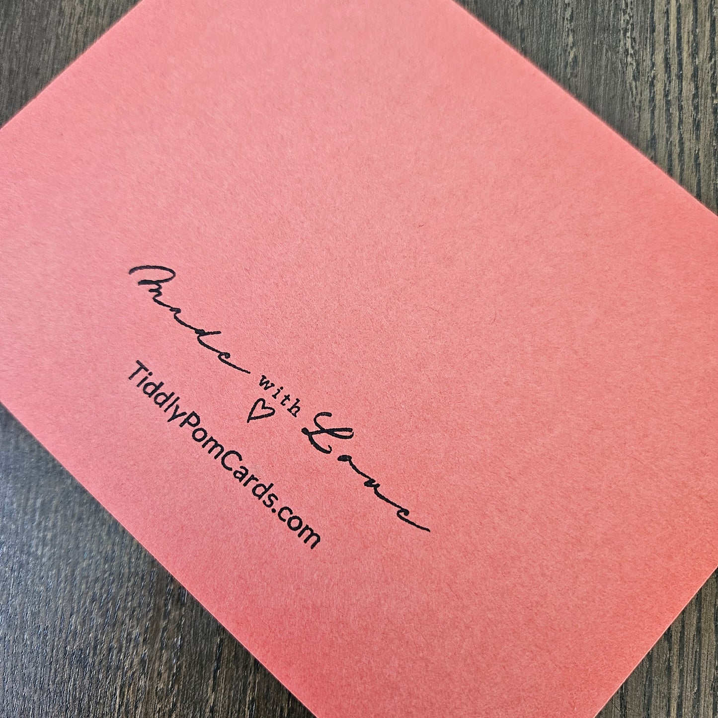 A coral pink textured card with black printed text reading 'Panda with Love', a small heart, and 'TiddlyPornCards.com', photographed on a dark wood surface.