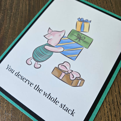 Front of a handmade A2 birthday card featuring classic Piglet balancing a stack of wrapped birthday gifts framed by black and green borders with text reading You deserve the whole stack.