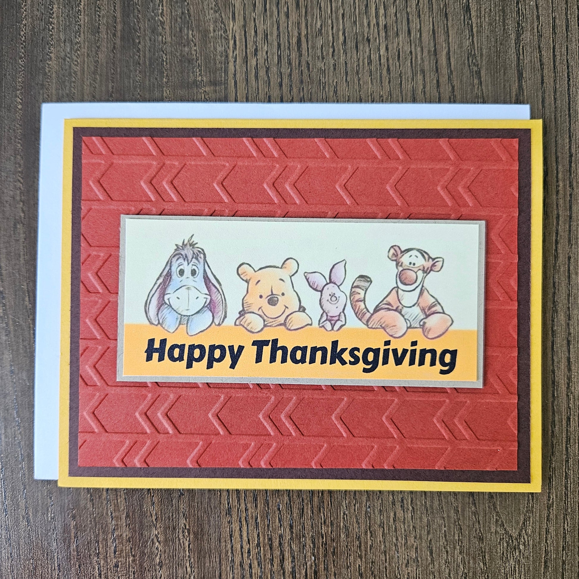 Front of a handmade A2 Thanksgiving card featuring classic Winnie the Pooh, Eeyore, Piglet, and Tigger on an embossed rust-red panel framed by yellow and brown borders with text reading Happy Thanksgiving.